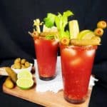 A Loaded Caesar Mocktail featuring various garnishes on a cutting board against a black background.