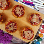 Cauliflower pizza bites on a wooden board surface on a table background with art supplies around it.