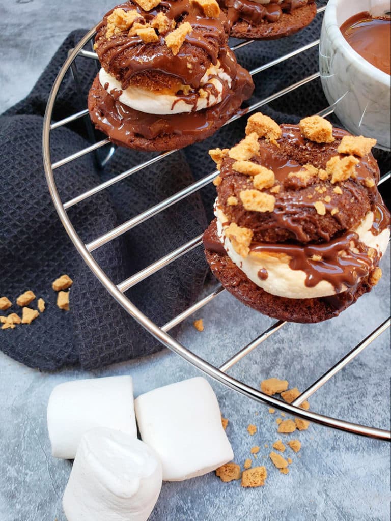 S'Mores mini donuts on a cooling rack with marshmallows and crack cracker crumbs on the counter top background.