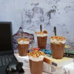 Chocolate Banana Chia Parfait on top of some books on a table with a laptop and wireless mouse. The background is a brick wall.