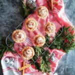 A top-down image of Mini Egg Nog Pies on a wire cooling rack. Below it is a red and white cloth and around it is Christmas decorations.