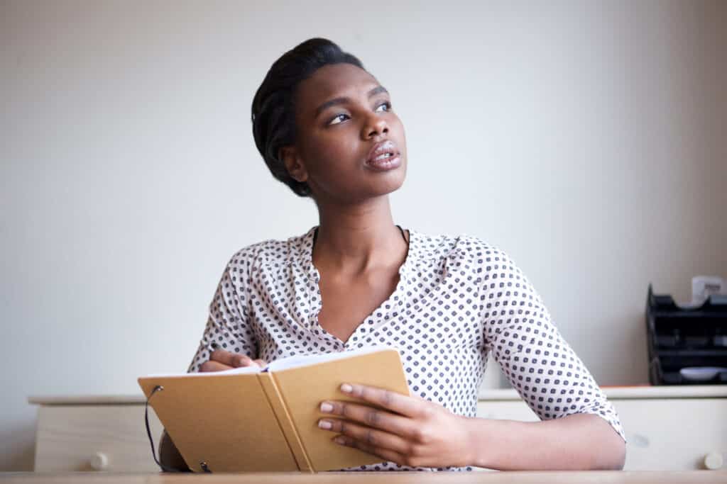 A portrait of a serious-looking young woman thinking and writing in journal.