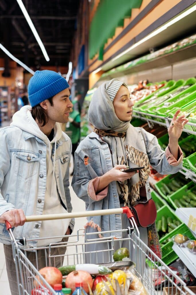 A man and a woman standing around a fridge display in a grocery store looking for produce.