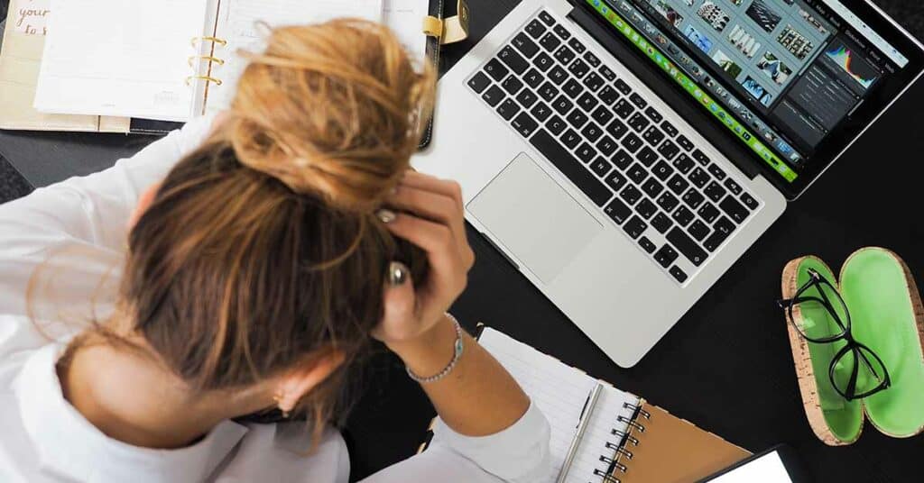 A woman holding her hands in her head while working on her laptop. She is visibly stressed.